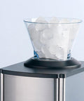 Contenitore trasparente pieno di cubetti di ghiaccio su tritaghiaccio elettrico con base nera e corpo in acciaio inox